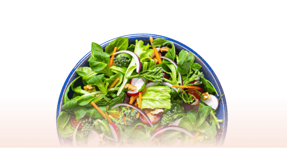 Fresh green salad in a blue bowl with mixed vegetables including spinach, carrots, radishes, and red onion slices.
