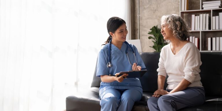 Healthcare professional sitting with an older adult and discussing information using a tablet in a home or clinic setting.